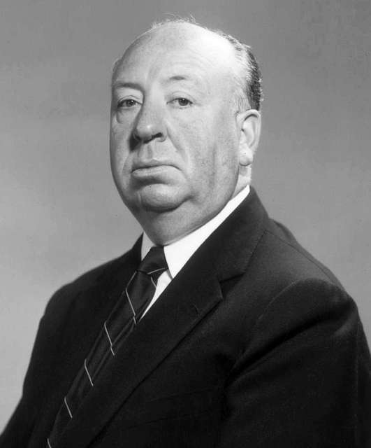 A black and white photograph of Alfred Hitchcock at a 3/4 angle looking at the camera seriously